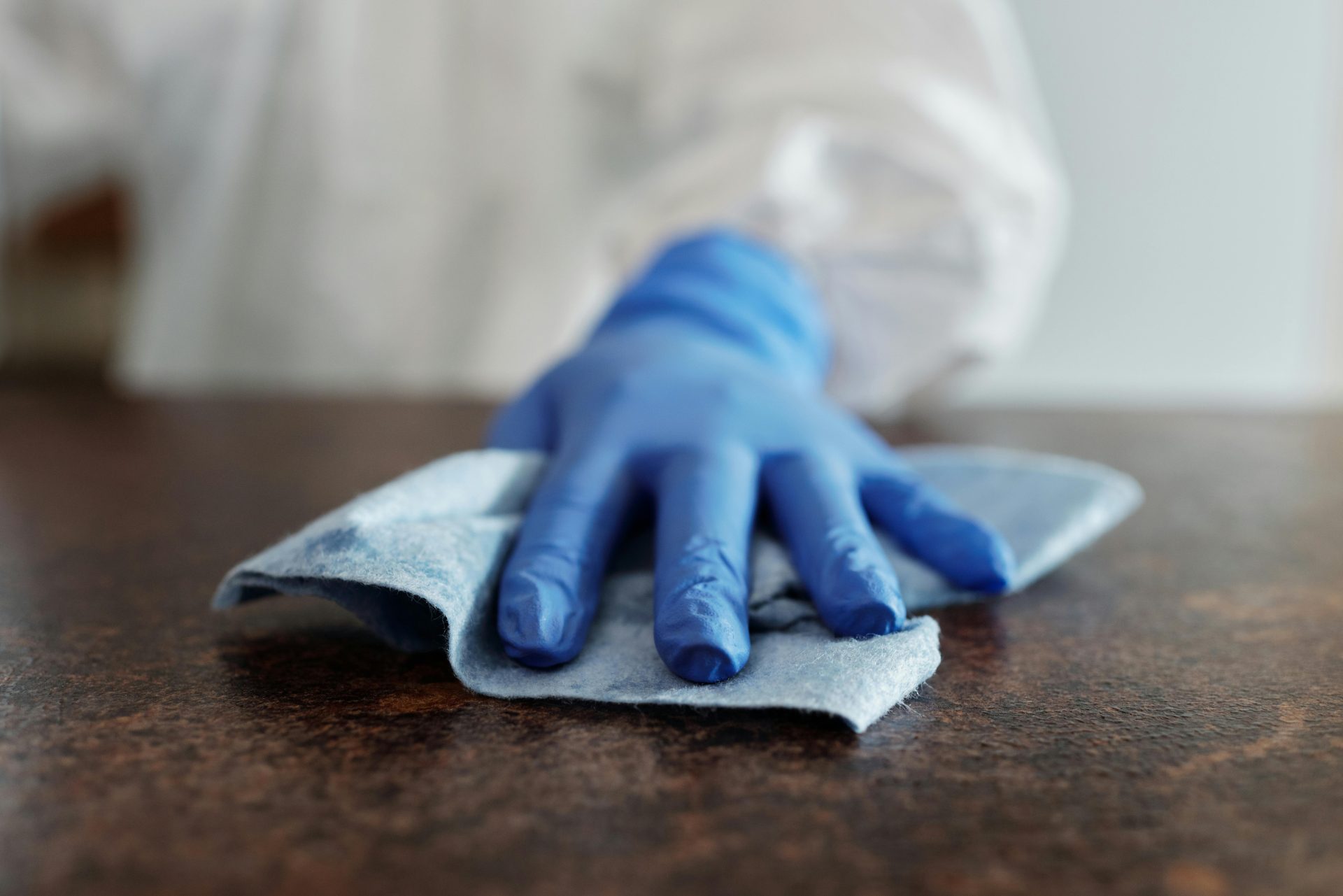 Eine Hand mit einem blauen Handschuh wischt eine Oberfläche mit einem Tuch ab und unterstreicht damit Hygiene und Sauberkeit.